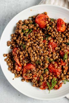 a white bowl filled with lentils and tomatoes on top of a table next to a napkin