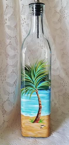 a glass bottle with a painting of a palm tree on the beach in front of a lace curtain