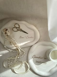 a pair of scissors sitting on top of a white plate next to a pearl necklace