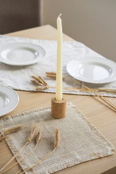 a candle is sitting on top of a placemat with wheat stalks and plates around it