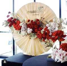 two vases with red and white flowers in front of a large fan on a table