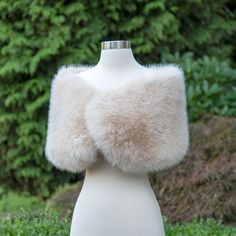 a white mannequin with a fur collar on it's head and bushes in the background