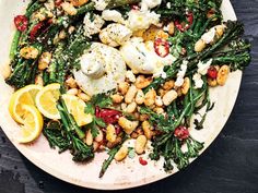 a white plate topped with green vegetables and chickpeas next to lemon wedges