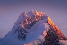 a snow covered mountain peak with the sun shining on it's side and clouds in the background