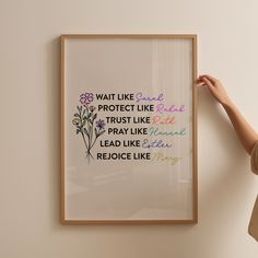 a woman holding up a framed art print with the words, wait like protect like trust like pray like lead like peace like rejoice like mary