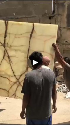 two men standing next to each other in front of a large slab of marble on the ground