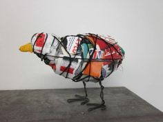 a bird made out of magazines sitting on top of a cement floor next to a white wall