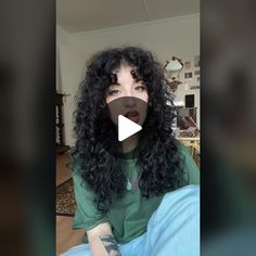 a woman with long black curly hair sitting on the floor