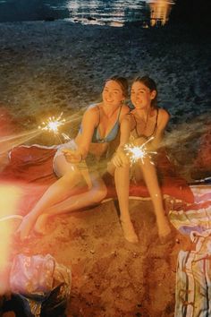 two women sitting on the beach with sparklers in their hands