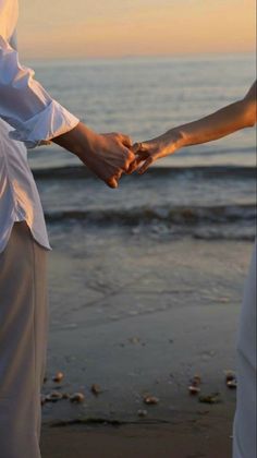 two people are holding hands on the beach