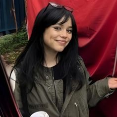 a woman with long black hair and sunglasses holding an umbrella in front of a red curtain