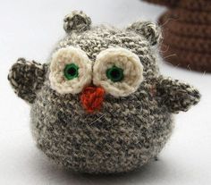 a knitted owl with green eyes sitting next to a crochet hat on a white surface