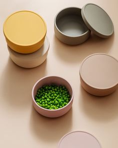 four bowls with peas in them sitting on a table next to one another and the other two are empty