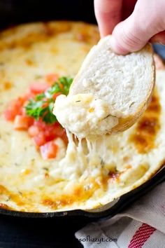 a hand holding a piece of bread over a skillet filled with cheese and vegetables