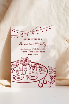 a red and white dinner party card sitting on top of a bed next to pillows