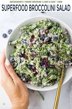 someone holding a bowl of broccoli salad with blueberries and cranberries