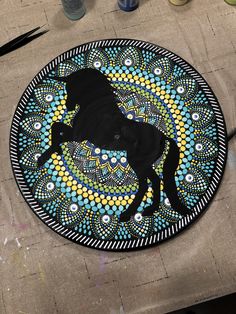 a black horse painted on top of a blue and yellow circular rug next to paintbrushes