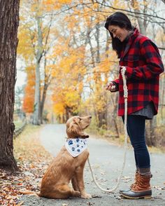 a woman wearing a bandana and holding a dog on a leash in the woods