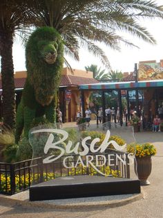 the bush garden sign is in front of some palm trees and people walking around it