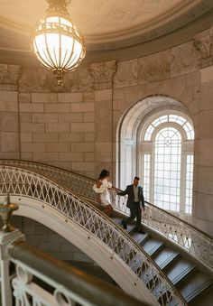 a man and woman are walking down the stairs in an old building with arched windows