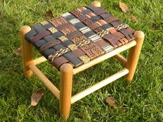 a small wooden stool with leather straps on it's legs in the green grass