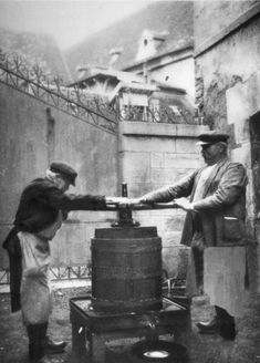 an old black and white photo of two men shaking hands over barrels in front of a building