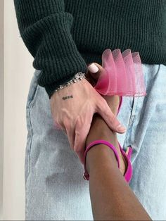 a man and woman holding hands while wearing matching pink sandals, bracelets and green sweater