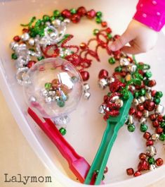 a child's hand holding a toothbrush next to beads and christmas decorations on a tray