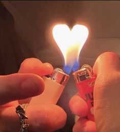 someone holding two lighters in their hands with a heart shaped light on top of them