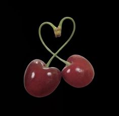 two cherries in the shape of a heart on a black background with green stems