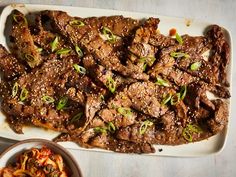 a platter filled with meat and vegetables next to a bowl of sauce on the side