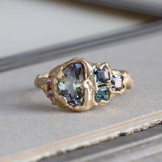 Our handmade tanzanite ring celebrates the unique particolor of this ethically sourced gemstone. An unusual crescent shape weighing 1.35 ct, the glittering ombre hues of green to purple are completely as Mother Nature intended: no-heat treatment for color or clarity with exceptionally energetic sparkle. Natural pink, purple and green spinel and twin pink Malaya garnet accents play to the ethereal and shifting colors of the main stone; the organic vibe is carried through with the textured branch-style band. An easy to wear low profile and measuring approximately 10.55 mm (about 3/8") north to south at the center front with a 2-3 mm average band width.  Currently size 6 3/4 and resizable at least two full sizes without issue. We can replicate the branch-like quality of the band at the sizing Organic Wedding Ring, Malaya Garnet, Branch Ring, Bohemian Bridal, Custom Gift Boxes, Crescent Shape, Tanzanite Ring, Purple And Green, Bangles Jewelry