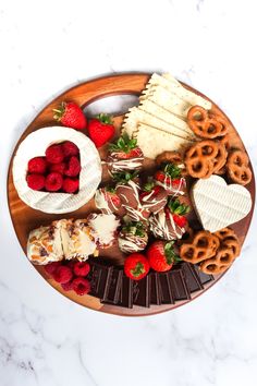 a wooden platter filled with cheese, strawberries and pretzels