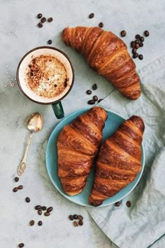 two croissants on a plate next to a cup of coffee and spoon