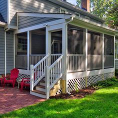 a porch with two chairs and a red chair on the grass next to a house