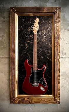 a red electric guitar in a wooden frame on a wall with a black background and some white speckles