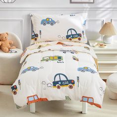 a child's bed with cars and trucks printed on the comforter, along with a teddy bear