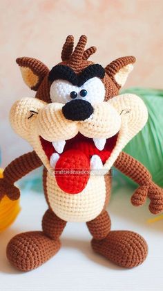 a crocheted stuffed animal with its mouth open and tongue out, standing next to yarn balls