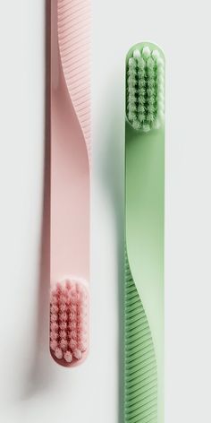 two toothbrushes sitting next to each other on a white surface, one with pink and green bristles