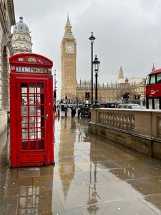 a red phone booth sitting on the side of a street next to a clock tower