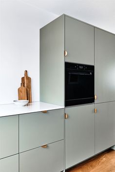 a kitchen with gray cabinets and white counter tops, wooden cutting board on the wall