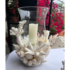 a glass vase filled with shells and a candle on top of a white table cloth