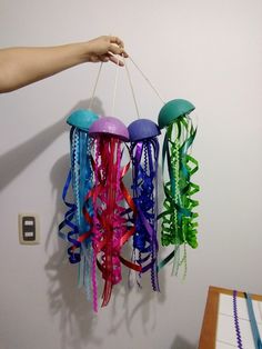 a hand is holding some colorful jellyfish hanging from a hook on the wall next to a table