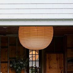 a large lamp hanging from the side of a wooden building next to flowers and potted plants