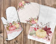 three kitchen towels and two oven mitts with pumpkins on them sitting on top of a wooden table