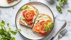 two slices of bread with tomatoes and cheese on them next to a fork and knife