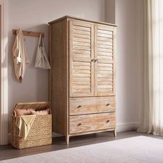 a wooden armoire next to a basket and coat rack in a room with white walls