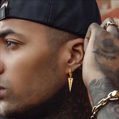 a man with tattoos and piercings on his arm wearing a black hat, gold chain earrings