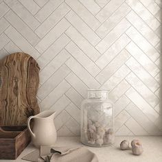 a kitchen counter with white tile on the wall and wooden cutting board next to it