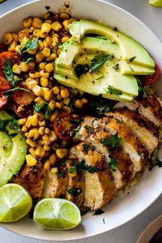 a white bowl filled with chicken, avocado, corn and sliced limes